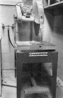 A 360-millimeter circular, diamond-edged blade with wide slotted teeth is mounted on a saw station bench. The blade is positioned vertically to allow the operator an easy sliding motion of the sample toward the blade. A large foot-pedal at the bottom of the bench controls the height of the saw.