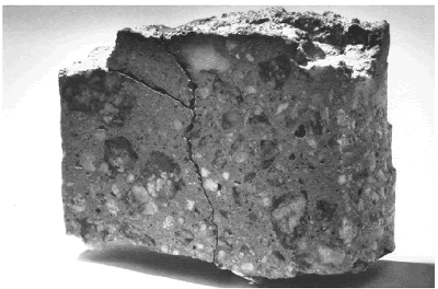 Plastic shrinkage cracking was covered up by mortar filling over it on top of a 100-millimeter core.  The top section of a broken concrete core is shown with areas of finer mortar material noticeable near the surface. The mortar was worked into surface plastic shrinkage cracks while the concrete was still plastic. These weaker areas of the hardened concrete cracked again. A near-vertical crack is shown with a crack branching off at a lower angle. Chunks of the top surface have broken off.