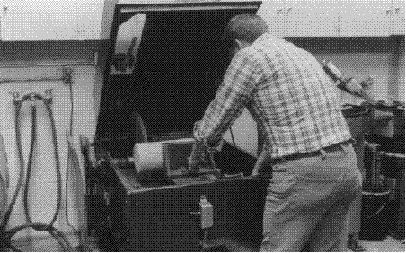 A man operating the saw provides a perspective on the size of the saw station; it is a little larger than a typical kitchen stove appliance. A cover encloses the entire unit to contain the splashing of oil.