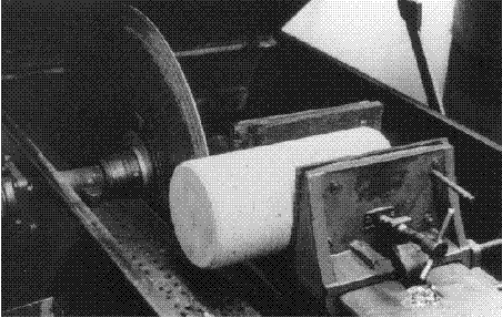 This is a closer view of the saw shown in figure 4. A smooth-edged blade (with no visible teeth) and a vise are mounted on a frame such that a clamped horizontal concrete cylinder or core will be cut vertically at any chosen point while the vise automatically pushes the cylinder toward the blade. An oil bath keeps the blade lubricated.