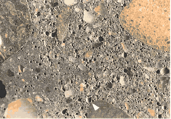 The concrete surface shown can be characterized by large numbers of voids of approximately 1 millimeter diameter as well as smaller voids. The area of darker paste (lower left) has a lower void content. If an H C C contains more than one kind of paste, this generally indicates that the mixture had begun to hydrate before additional water was added. The void content of this concrete is much greater than the upper limit of the specification range. An example 1 millimeter void is shown marked with an arrow.