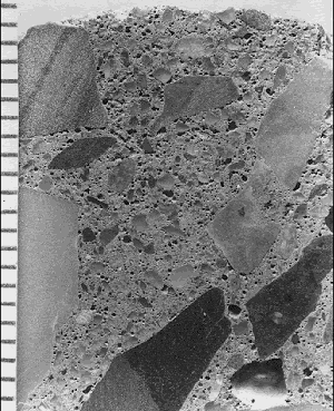 This cross section of a concrete core is representative of a placement in which water was added to facilitate the finishing. It shows elongated, angular coarse aggregate, which caused the mixture to be difficult to place. Angular voids are present to a depth of 10 millimeter. The deteriorated, originally finished surface is at the top of the picture.