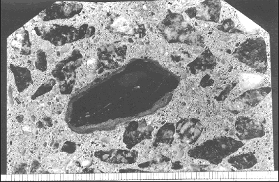 A polished surface of concrete shows a piece of coarse aggregate that is coated with cement that is not hydrated. This occurred because the aggregate was damp and came in contact with dry cement. This layer is much denser than the zone surrounding the aggregate in figure 54.