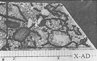 This lapped surface is closely related to the one shown in figure 83 on the same page. Each one is approximately 25 by 50 millimeters. Both have been marked with ink to establish boundaries on portions of interest. The cracks have been marked as well. This sample contains an experimental admixture that caused a greater number of cracks, particularly around aggregate particles