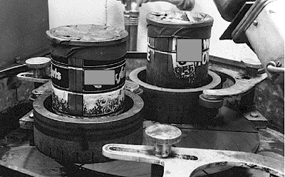 Photo focuses on two of the specimen-holder rings in the previous figure. Here, ordinary coffee cans, filled with lead shot, have been inserted into each ring to keep the samples pressed against the horizontal lap wheel.