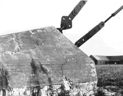 Photo shows a massive concrete anchor block for support cables that has experienced significant cracking in random directions