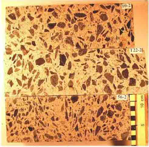 Photo. Polished surfaces of three concrete cores. The size, shape and color of the coarse aggregate particles and their distribution are shown. Photograph by Dr. P.E. Grattan-Bellew. This photo shows three concrete cores cut lengthwise. The cores are labeled, starting from the top, 10-2, T22-2, and 56-2. A metric scale is shown next to the third core sample and illustrates that the diameter of the core is near 10 centimeters wide (near 4 inches). The aggregates in the samples are clearly shown in all three samples.