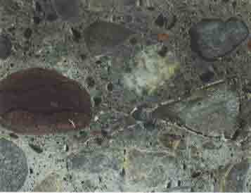 Photo. An example of a polished concrete surface. This photo shows a microscopic view of a polished concrete surface. The aggregate particles along with small vertical cracking can be seen.