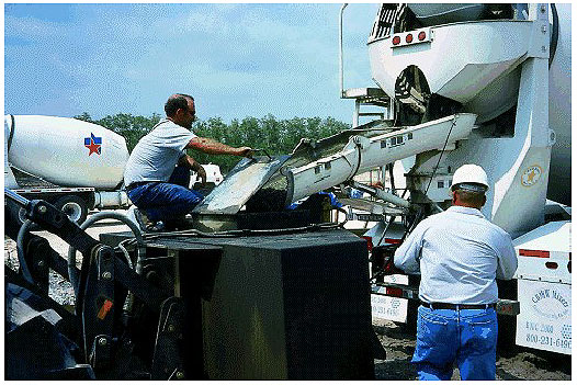 Figure 30.  Photo. Utility Transmission Tower Footing in Corpus Christi, TX. This photo shows two workers pouring concrete.