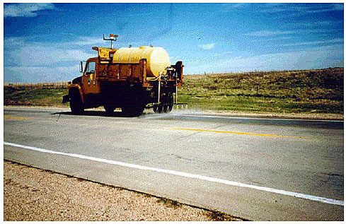 Figure 32.  Photo. Topical Application of a Pavement near Wolsey, SD. This photo shows a truck spraying solution onto the pavement.