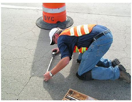 Figure 37. Photo. Making Length-Change Measurements on a Treated Pavement in Mountain Home, Idaho. This photo shows one of the research team members taking expansion measurements using a gage reader on a treated section of pavement.