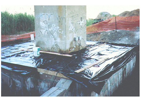 Figure 39. Photo. Application of an Electrochemical Lithium Migration Technique for a Pier Footing on the New Jersey Turnpike. Two devices are fastened to the side of the footing, and the base is covered with a tarp.