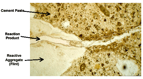 Figure 5.  Enlarged Photo. Thin-Section Cut of ASR-Damaged Concrete, Showing ASR Gel and Typical Crack Pattern (Through Aggregate and into Surrounding Matrix). This photo shows cement paste, a particle of reactive aggregate (in this case, flint), and a ribbon of reaction product (alkali-silica reaction gel) running through both of them.  A crack runs from a point where the gel meets the cement paste and continues parallel to the gel.
