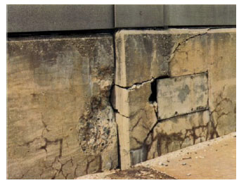 Figure 8.  Photo. Misalignment of Adjacent Sections of a Parapet Wall on a Highway Bridge Due to ASR-Induced Expansion (SHRP-315, 1994). This figure shows the misalignment of adjacent sections of a parapet wall on a highway bridge.  Although there is no scale, the lateral misalignment could be on the order of several centimeters. Both sections contain horizontal and vertical cracks.