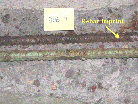 Figure 30. Typical condition of ECR with poor performance (slab #30-top right bar). Photo. The picture shows an ECR concrete slab with a severely corroded ECR. The concrete interface shown above the ECR sample is completely covered with corrosion product. The ECR is mottled green with some rust and discolored spots and is separated from the concrete. The label reads 30B-T.