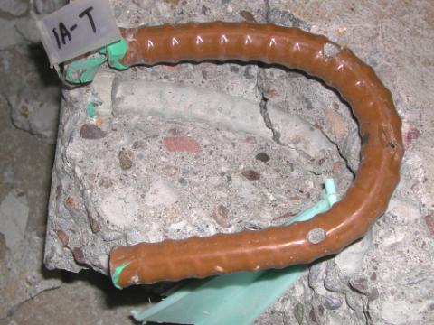 Figure 31. Typical condition of a bent ECR with good performance (slab #1-top left bar). Photo. The picture shows a bent gold-colored ECR labeled 1A-T extracted from a concrete slab. The concrete and bar are in good condition with no evidence of discoloration or corrosion.