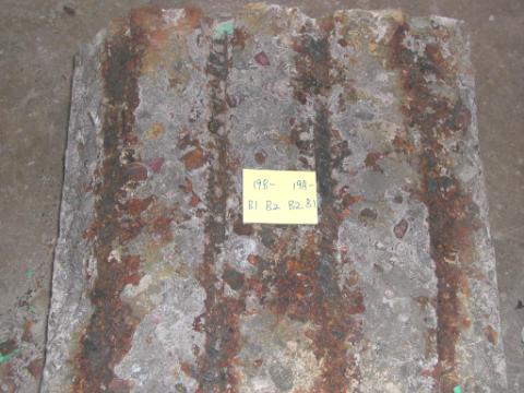 Figure 36. Corroded bottom mat (slab #19). Photo. The corroded bottom mat shows four grooves that held bars designated B1, B2, B3 and B4. Two top mat ECRs labeled 19B and 19A had been connected to these bars in the bottom mat. The grooves as well as the area around them are discolored and covered with corrosion products.