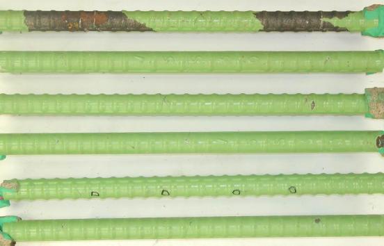 Figure 38. Photograph of autopsied bars extracted from slab #10 (ECRs in both mats). Photo. The bars in this photo show typical condition of well performing ECRs in the top mat. Four bottom mat ECRs are also shown at the bottom of the photo. They retain original green coating. The top bar is the most delaminated with some rust spots showing. The second bar up from the bottom shows four intentional coating defects.