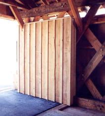 The picture shows a bridge interior with a shelter panel of vertical board and batten construction that wraps around and continues on the inside to cover the trusses at the ends of the bridge. Shelter panels act as portal siding to protect the end truss members from wind-borne rain and vehicle splashing.