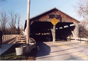 This double-barrelled bridge still supports two lanes of traffic. It features a third truss between the roadways and an approach railing with warning signs posted on its portal. The sidewalk on the left side is a more recent addition.