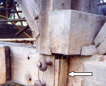 This picture shows a white arrow pointing to a wedge located on the bottom chord of a Long truss. The wedge takes some of the bearing load and has large metal bolts in it.
