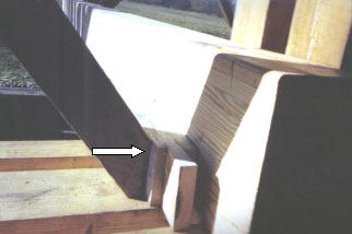 This picture shows a white arrow pointing to a block of wood between a thick floor beam and a diagonal counter member.
