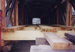 This picture shows the inside of a bridge rehabilitation where the glue-laminated floor beams and decking system are under construction. These systems are pre-fabricated deck panels (40 meters (130 feet) in this example) that have higher allowable stresses and are oriented longitudinally along the bridge, installed staggered so the butt joints of adjacent panels are supported on different floor beams.