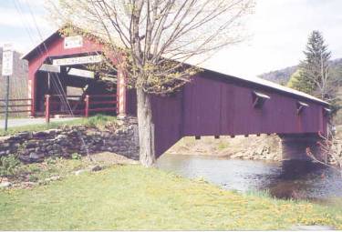 The gable or peaked roof is the most common style of covered bridge. The picture shows a bridge side view with the approach guide rails and stone foundations, wood shutter windows and a classic gable roof with a moderate pitch.