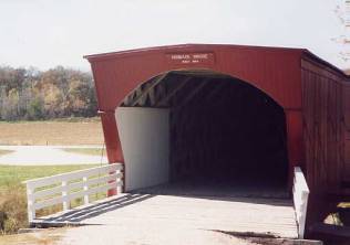 The picture shows a bridge entrance with a flat roof a bit wider than the side walls. The portal is arched with an inside shelter panel and the approach rails are three-tiered white.