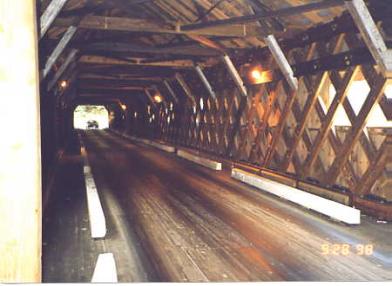 The interior of this Town lattice truss bridge shows white concrete beams on both sides that act as curb traffic protection, which is a prudent and practical way to rehabilitate covered bridges.