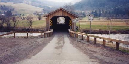 The picture shows the entrance to a bridge with a 3-ton weight limit sign. The "squeeze" timber approach railing narrows in before the bridge entrance to prevent larger vehicles passing through and forcing slower speeds.