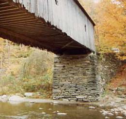 This picture shows the underside of a bridge with the original stone abutment in good condition with the base somewhat wider than the top where the bridge sits. The stones are laid dry without mortar.