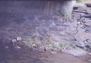 The picture shows an abutment where stones still show on the right side but the majority of the stonework is hidden by pointing the stones with mortar, then parging the surface with a thin layer of concrete.