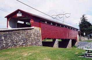 The picture shows a side view of a bridge with stone approach railing, abutment and two piers. The bridge has painted siding in a dark color. Surface treatment means maintenance during the life of the siding with more of an aesthetic than longevity value.