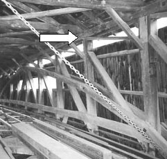 The picture shows the interior of a Burr arch bridge. The white arrow points to an upper joint between the sides and the roof of the bridge. This configuration is unconventional in that the diagonals intercept the posts at a distance from the top chord (and bottom chord also which is harder to see.)