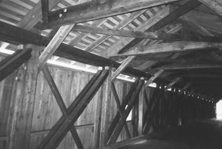 This interior view shows a more substantial upper bracing system featuring cross laterals, heavy tie beams, and strong knee brace frames connected to a heavy collar tie near the roof peak. Heavy bolts tie all these members together.