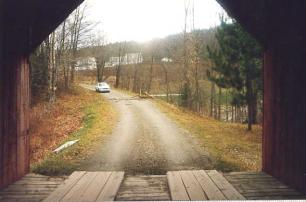 This view taken from inside the bridge shows the l portal and a car on the approach road. Two sets of four flat boards that correspond to the wearing surface where vehicles travel are the running planks.