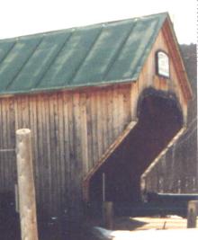 The picture shows a side view of a Town lattice bridge with an inclined end treatment at the entrance that follows the line of the lattice. The wextension appears to be cantilevered out so that the roof and upper sides are extended and protect the bridge entrance from the elements.