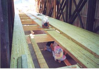 The picture shows an opening in the floor of the bridge with a worker installing stronger glue-laminated members. All the lighter-colored wood is the laminated transverse floor beams and full-length deck panels.