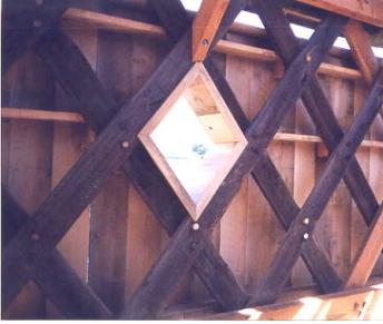 Windows give interior illumination but the details can be critical for drainage and protection to avoid premature truss deterioration around them. The picture shows a diamond window that is an opening cut-out from the intersection of the lattice pattern. Lighter-colored wood siding lines the opening.