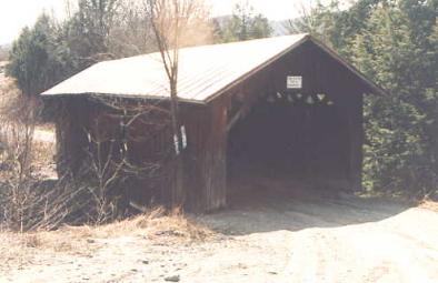 The picture shows the outside view of a bridge. The approach grading is such that the road is higher and slopes directly into the bridge without a way to channel the water from entering the bridge.