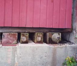 Since covered bridges deteriorate if they come in direct contact with foundation materials from poorly drained rainwater at the abutments or condensed dew on the masonry, sacrificial timbers can protect the truss members and end floor beams. The picture shows pressure-treated sacrificial timber blocking beneath the main truss.