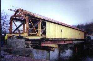 Figure 179 Successful relocation of the Downsville Bridge using rollers on a false work system. The falsework appears to be steel stringers on temporary bents. The siding and roofing at the ends awaits final bearing installation. Photo.