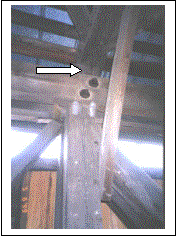 Figure 183 Diagonal to post connections at the top chord indicating significant overstress. If you look carefully you see that the top of the vertical post is cracked above the upper right bolt. Also note the general bend of the vertical to the right. The knee brace is in the foreground connecting to the tie beam just out of the top of the photograph. The pair of main diagonals is on the right and the counter is on the left. The reconstruction of the bridge replaced these split posts with heavier members. The picture is hard to see clearly. Photo.