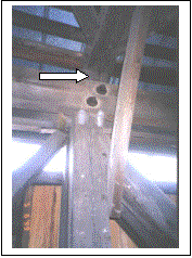 Figure 183 Diagonal to post connections at the top chord indicating significant overstress. If you look carefully you see that the top of the vertical post is cracked above the upper right bolt. Also note the general bend of the vertical to the right. The knee brace is in the foreground connecting to the tie beam just out of the top of the photograph. The pair of main diagonals is on the right and the counter is on the left. The reconstruction of the bridge replaced these split posts with heavier members. The picture is hard to see clearly. Photo.