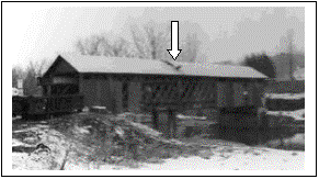 The picture is a blurry image of Fitch's Bridge, a Town lattice truss bridge. The white arrow points to the hole in the roof and the siding removal to allow installation of steel piles to support the falsework system
