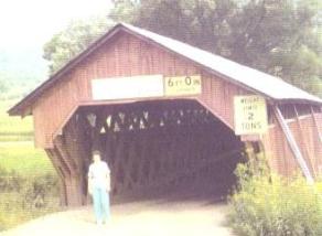 The blurry picture shows a woman standing in the entry to the bridge. The interior decking appears sloped downward because the original floor was hung beneath the lower chord with iron rods and a ramp floor that transitions to a floor at the correct elevation supported beneath the lower bottom chords.