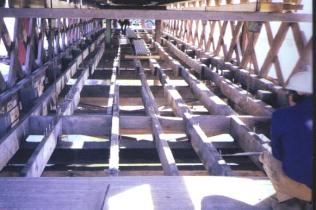 The picture shows partial removal of the floor beams (2-meter or 8-foot spacing) and longitudinal stringers with an irregular 0.61-meter (2-foot) spacing. The near edge of the floor is the transverse nail-laminated decking.
