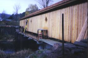 The bridge was previously covered with vertical rough-cut siding without battens. The picture shows a side view with battens used to lessen weather damage to the truss components.
