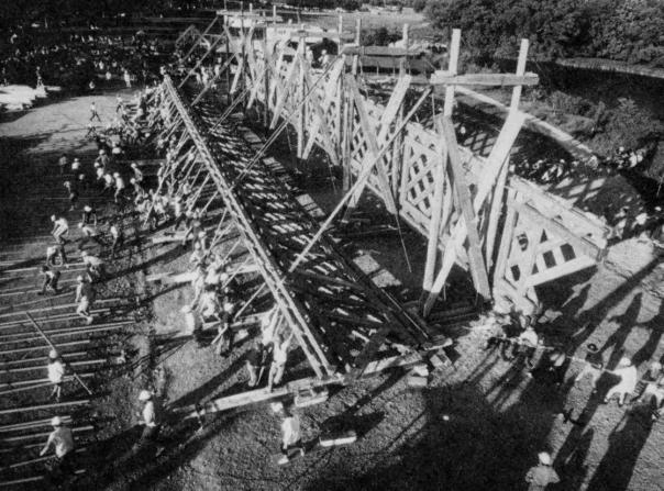 The picture shows the volunteer crew working in tandem to lift the truss by hand with traditional pike poles. The pullers hauled using manila lines with block and tackle rigged to phone pole derricks.